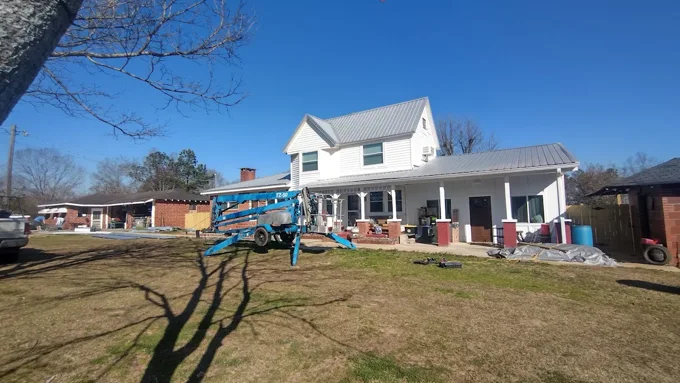 Metal-roofed farmhouse with a lift and equipment in the yard