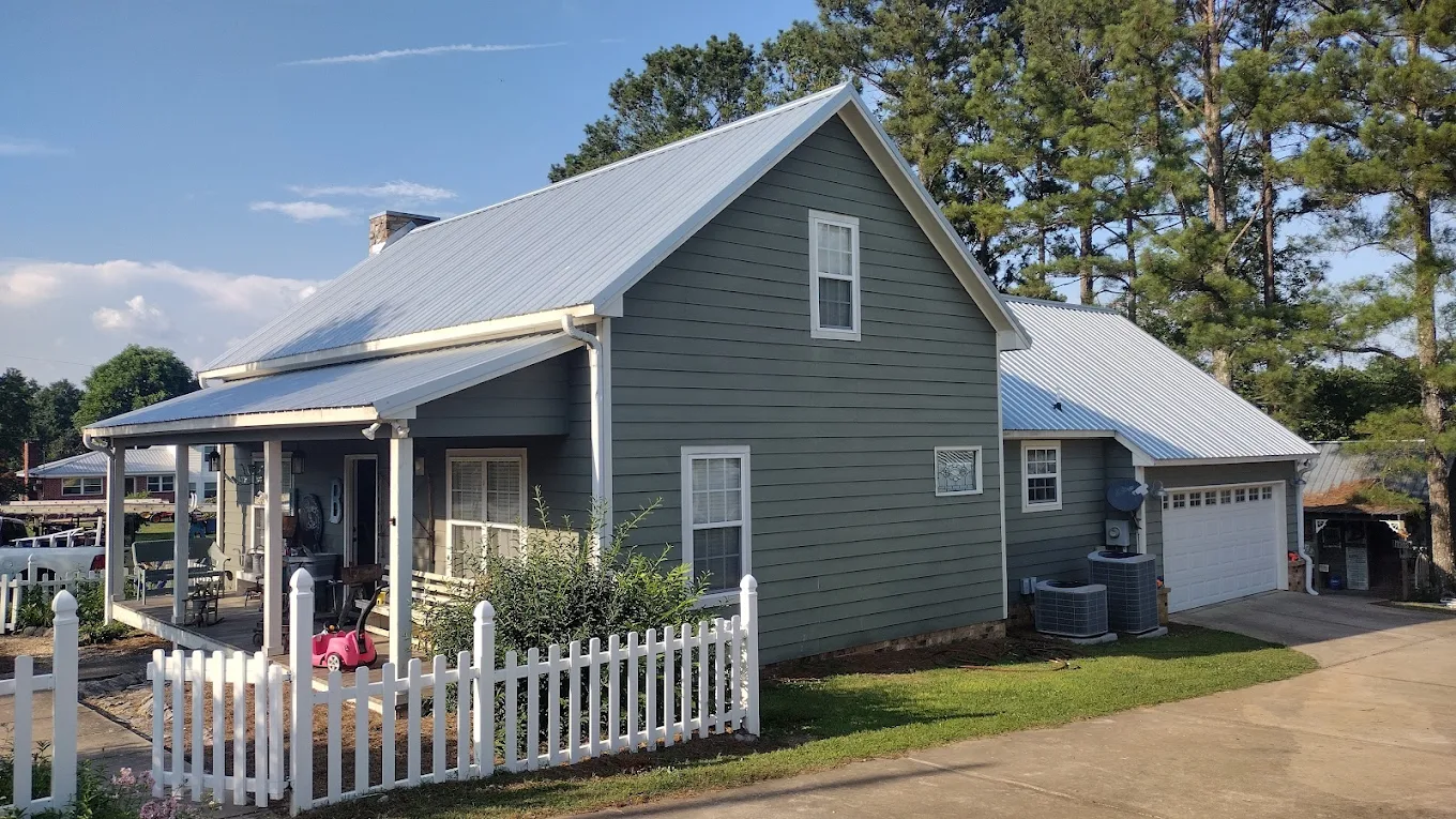 Silver metal roof over a gray home with a white picket fence